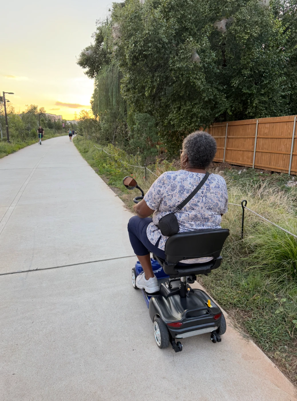 A rider on a blue mobility scooter cruising the BeltLine path at sunset, seen from behind.