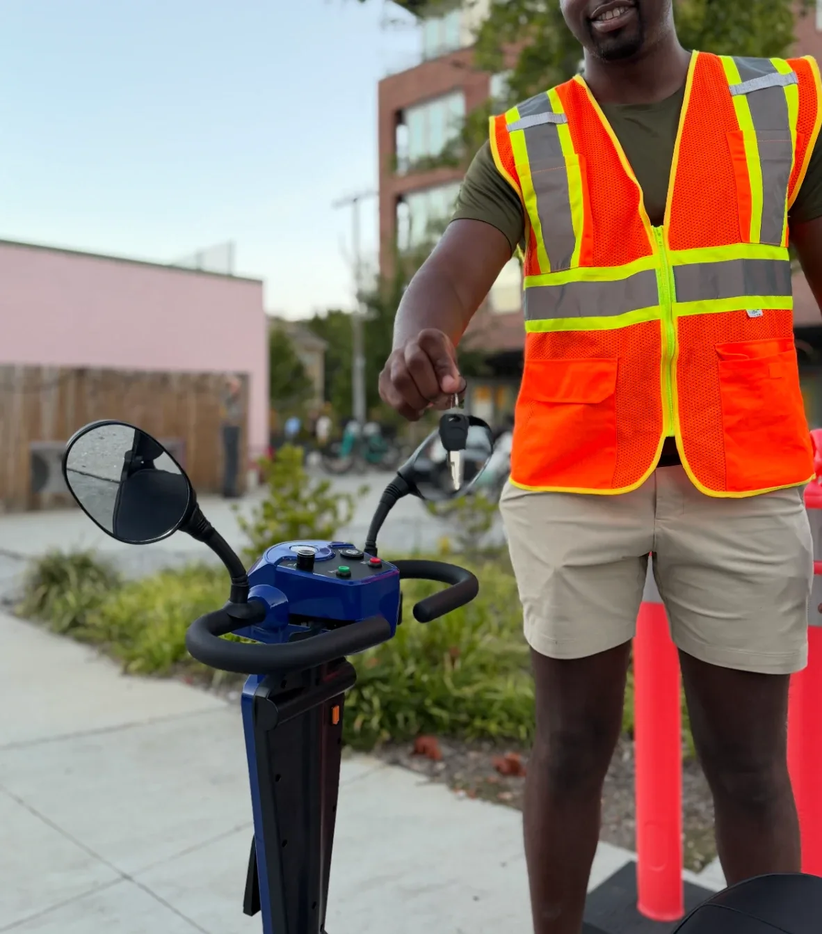 A JOY staff member in a safety vest holding out the key to a Joy Cruiser at pickup.